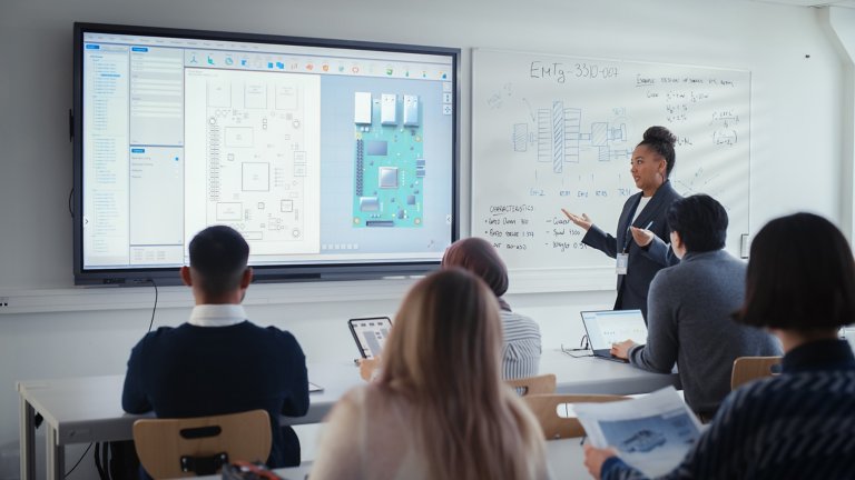一位黑人女教师使用数字互动屏幕向多元的学员群体演示课程，并展示 3D 电路板组件。教育