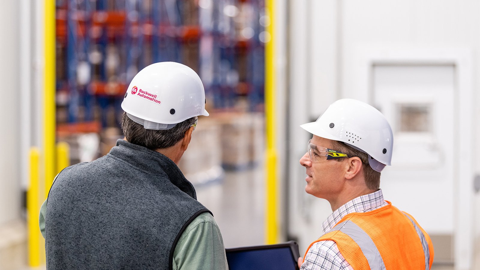 佩戴安全帽的 Rockwell Automation 顾问查看身穿橙色背心的男性客户的平板电脑